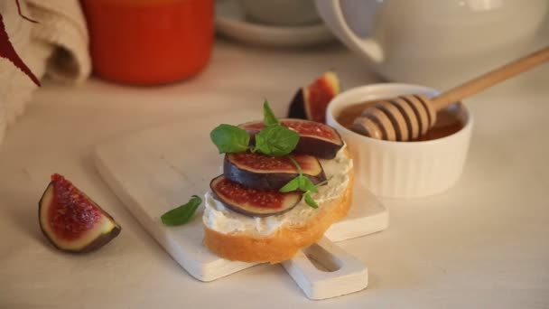 Mano de mujer poner en el sándwich de tabla de cortar blanco con queso crema, higos y miel. Concepto de comida saludable — Vídeo de stock