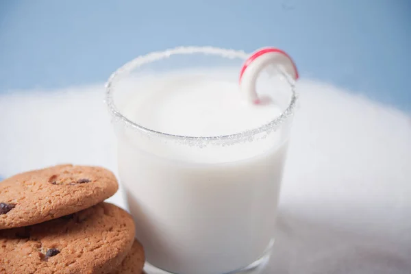 Glass of milk, candy cane, homemade cookies and snow on the blue background