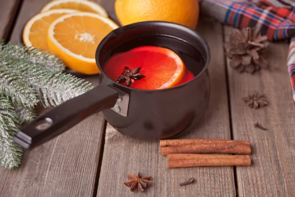 Old metal pan pot of tasty mulled wine with pot with spices and orange fruits on wooden table. — Stock Photo, Image