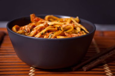 Kasede tavuk etli Udon eriştesi ve siyah taş arka planda çubuklar..