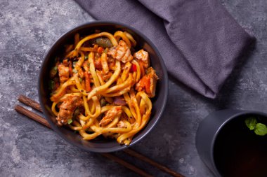 Udon eriştesi ve kase içinde tavuk eti, koyu taştan arka planda. Üst görünüm.