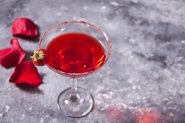Красный экзотический алкогольный коктейль в прозрачном стакане и красные розы лепестки на бетоне для романтического ужина. Копирование пространства . — стоковое фото