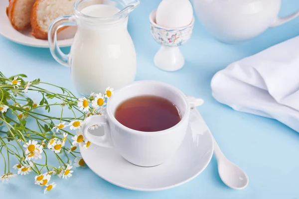 Bom dia. Pequeno-almoço. Xícara de chá com jarra com leite, ovo no fundo azul — Fotografia de Stock