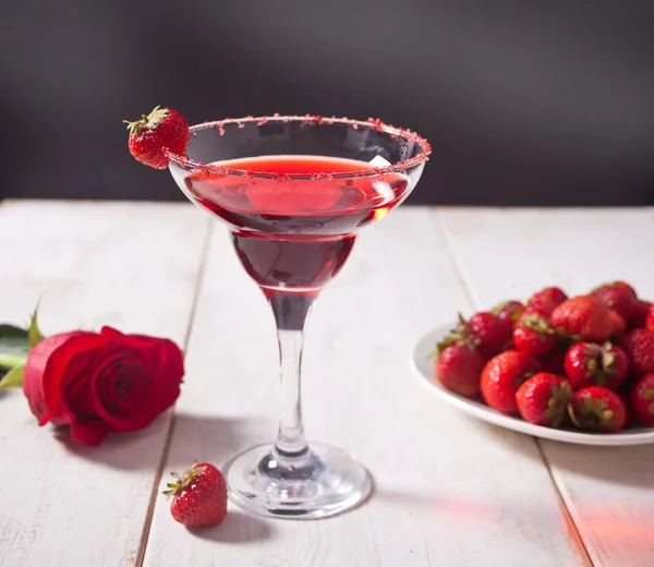 Red exotic alcoholic cocktail in clear glass, plate with fresh strawberries and red rose on the wooden white table for romantic dinner. — 스톡 사진