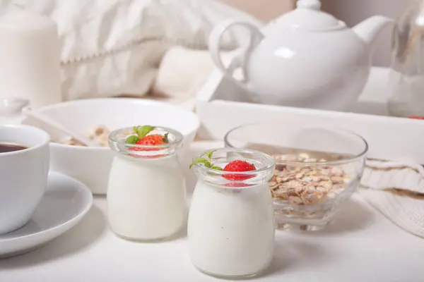 Две порции натурального домашнего йогурта в стеклянной банке со свежей клубникой и мюсли, чайник, чашка кофе поблизости. Концепция . — стоковое фото