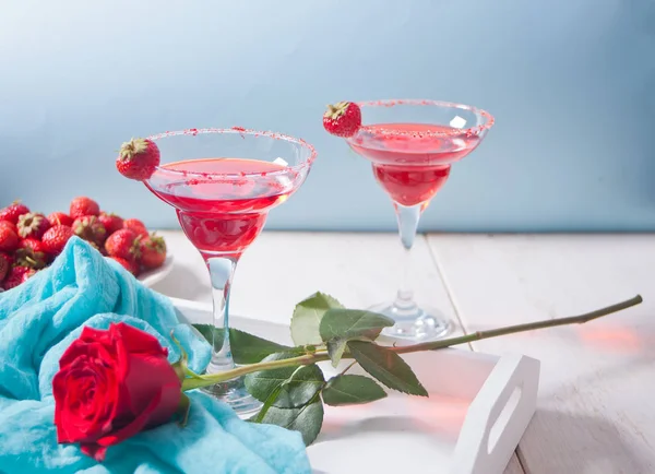 Červený exotický alkoholický koktejl v čirých brýlích a červené růži na dřevěném bílém podnose k romantické večeři. — Stock fotografie
