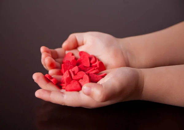 Mani del bambino che tengono i cuori rossi sullo sfondo nero . — Foto Stock