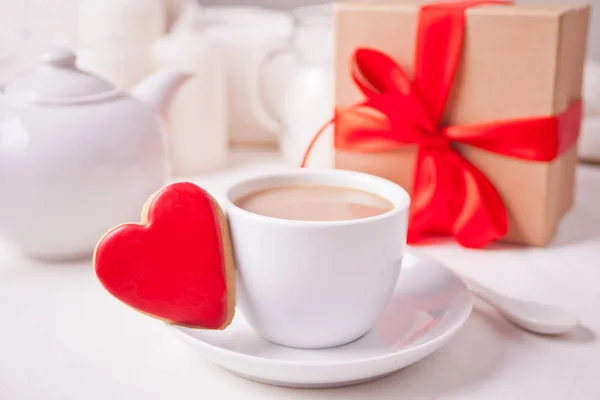 Чашка кофе и сердце форме красное печенье с подарочной коробкой и чайник на белом столе — стоковое фото