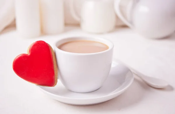 Чашка кофе и красное печенье в форме сердца с чайником, кувшин молока, свечи на белом столе — стоковое фото