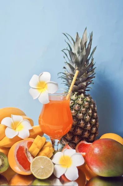 Glass of tropical exotic multifruit juice cocktail with frangipani flower and fruits on the background — 스톡 사진