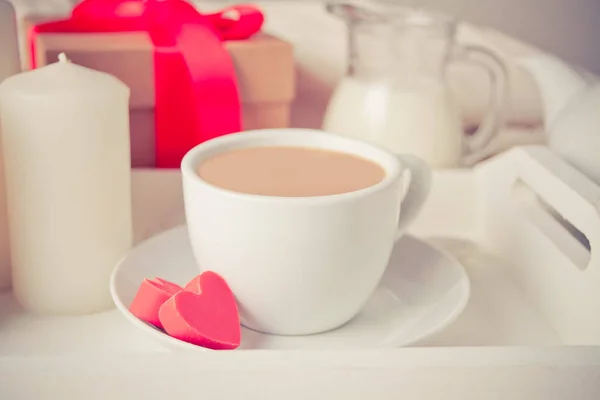 Чашка кофе и конфеты в форме сердца с подарочной коробкой на белом подносе — стоковое фото