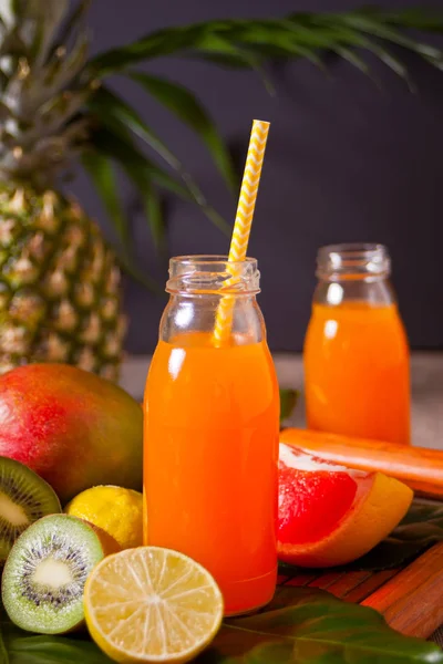 Dos botellas de jugo tropical exótico multifrutal bajo una palmera con frutas en el fondo . — Foto de Stock