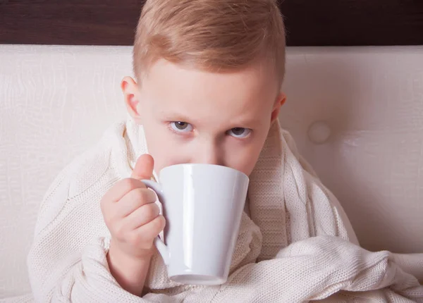 Nemocné dítě sedí v posteli a drží šálek čaje. Koncepce medicíny. — Stock fotografie