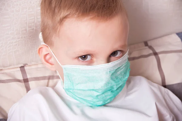 Sick boy sitting in bed in medical mask and doesn t feel well — 스톡 사진