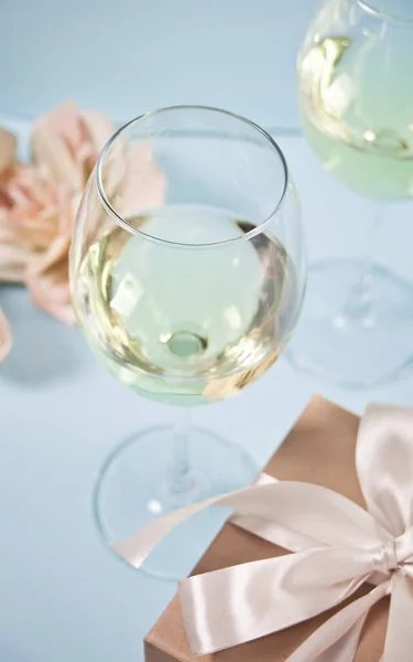 Due bicchieri di vino bianco con rose e confezione regalo sullo sfondo. Concetto di cena romantica . — Foto Stock