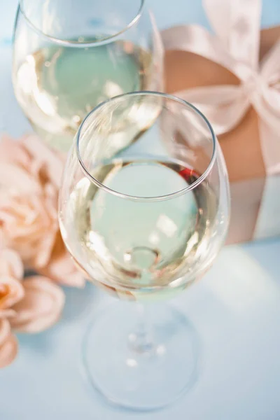 Due bicchieri di vino bianco con rose e confezione regalo sullo sfondo. Concetto di cena romantica . — Foto Stock