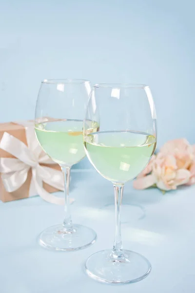 Two glasses with white grape wine with roses and gift box on the background. Romantic dinner concept.