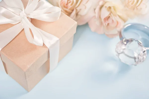 Caixa de presente com flores rosas bege e grande anel de diamante no fundo. Espaço de cópia — Fotografia de Stock