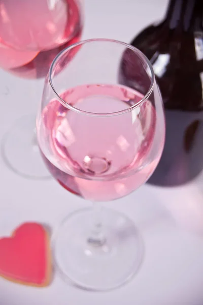 Två glas med rosa druvvin med hjärtformad kaka och flaska på bakgrunden. Romantiskt middagskoncept. — Stockfoto