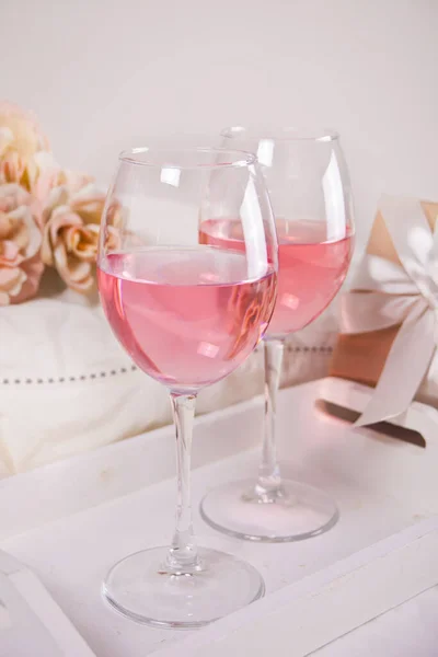 Dos copas con vino de uva rosa con flores y caja de regalo en el fondo. Concepto de cena romántica . —  Fotos de Stock