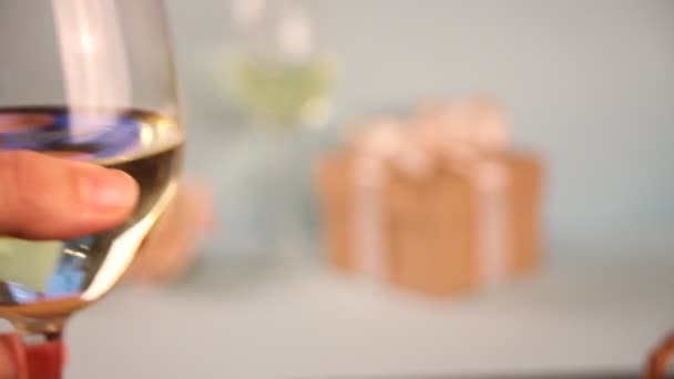 女性の手は白ブドウワインとガラスを保持します。背景にギフトボックス。ロマンチックなディナーコンセプト. — ストック動画