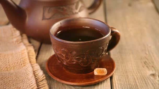 Someone put candy rock sugar in a cup of tea on the wooden table. Teapot on the background. — Stock Video