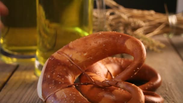 Vrouw hand neemt een vers gebakken zelfgebakken zout Beierse pretzel. Vlakbij staan twee glazen bier op de houten tafel. — Stockvideo