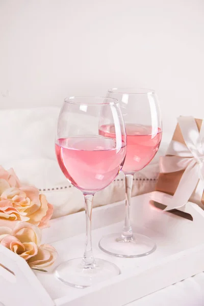背景にはピンクのブドウワインと花とギフトボックス付きの2つのグラス。ロマンチックなディナーコンセプト. — ストック写真