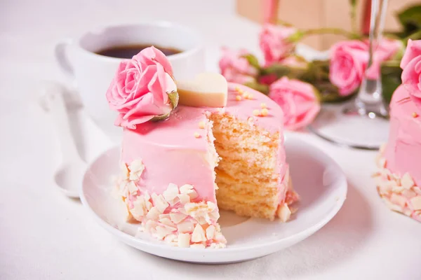 Mini petit gâteau avec glaçure rose, belles roses, tasse de café, boîte cadeau sur la table blanche . — Photo