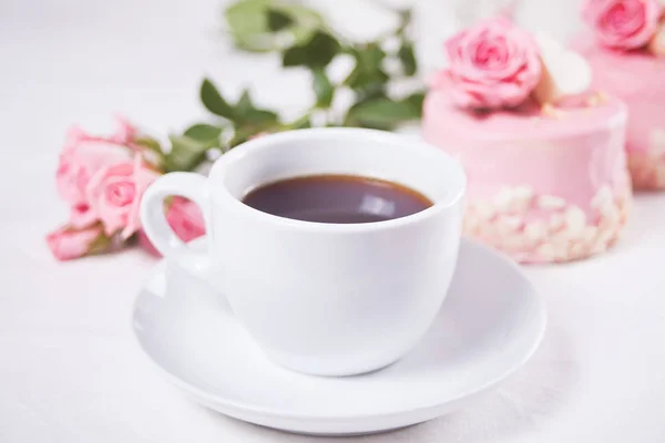 A cup of coffee, pink roses and small cake on the white table — Stock Photo, Image