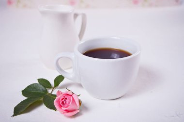 Beyaz masada bir fincan çay ve pembe güller