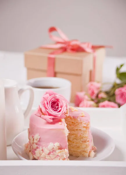 Mini pequeño pastel con esmalte rosa, hermosas rosas, taza de café, caja de regalo en la mesa blanca . — Foto de Stock