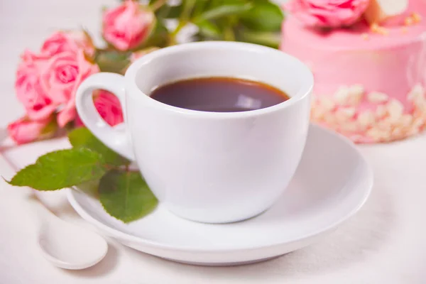 Чашка чая, розовые розы и маленький торт на белом столе — стоковое фото