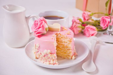 Pembe jöleli mini kek, güzel güller, bir fincan kahve, beyaz masadaki hediye kutusu.