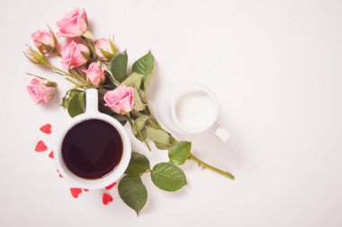 Beyaz masada bir fincan çay, süt ve pembe güller. Üst Manzara. Boşluğu kopyala.