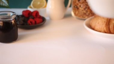 Kadın eli masaya böğürtlenli meyve suyu kasesi koydu. Kruvasan çöreği, yakınlarda bir bardak kahve