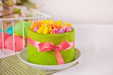 Bahar Paskalya Festivali masası. Tereyağlı kremalı küçük yeşil pasta ve arka planda renkli yumurtalar.
