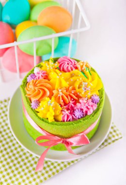 Bahar Paskalya Festivali masası. Tereyağlı kremalı küçük yeşil pasta ve arka planda renkli yumurtalar.