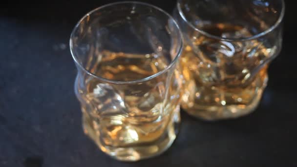 Dos vasos de whisky con hielo sobre una mesa negra . — Vídeos de Stock