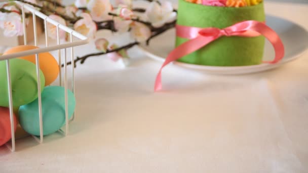 Mesa festiva de Pascua de primavera. Pastel verde pequeño con flores de crema de mantequilla y huevos de colores en el fondo. Mano de mujer poner una taza de té o café en la mesa . — Vídeo de stock