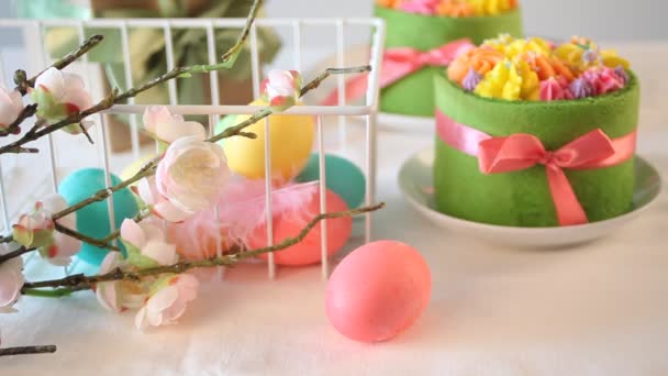 Ανοιξιάτικο τραπέζι Πάσχα. Μικρό πράσινο κέικ με λουλούδια κρέμας βουτύρου και πολύχρωμα αυγά στο παρασκήνιο. Πολύχρωμα πασχαλινά αυγά κυλούν στο τραπέζι. — Αρχείο Βίντεο