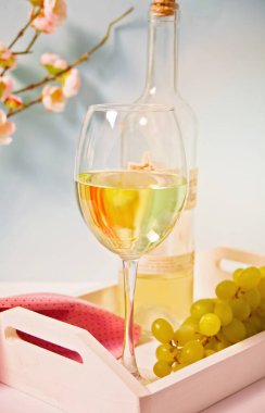 Çiçek açan bir dalın altında üzümlü beyaz üzüm şarabı olan cam ve şişe. Romantik bahar yemeği konsepti