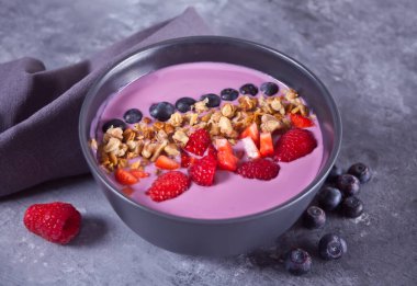 Meyveli meyve suyu kasesi ve gri masada müsli.