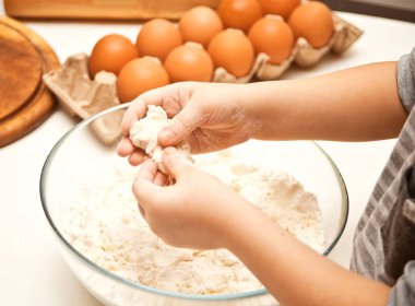 Küçük çocuk mutfakta pizza ya da başka bir yemek için hamur hazırlıyor.