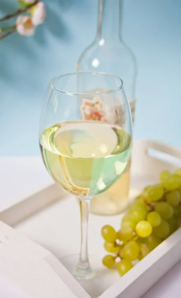 Glass and bottle with white grape wine with grapes under a blooming branch. Romantic spring dinner concept