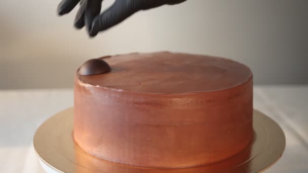 Frau Hand in schwarzen Handschuhen verziert Bonbons Schokoladenkuchen. — Stockvideo