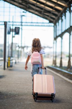 Kız tren gelmeden önce sırt çantası ve bavuluyla istasyona doğru yürür.