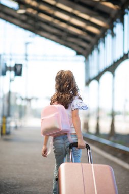 Kız tren gelmeden önce sırt çantası ve bavuluyla istasyona doğru yürür.