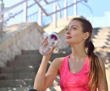 Güneşli bir günde açık havada su içen sportif bir kadın.