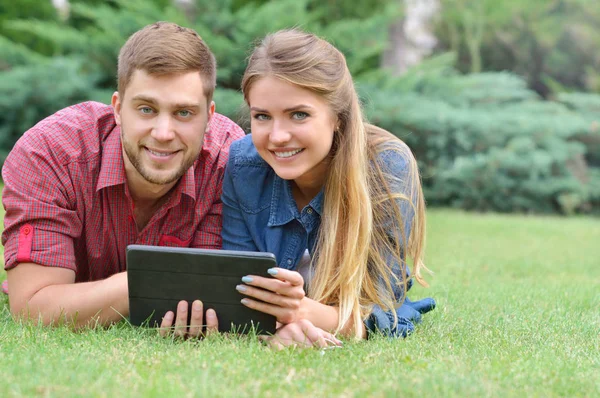 Couple lying in park using tablet pc together on a sunny day — Stock Photo, Image